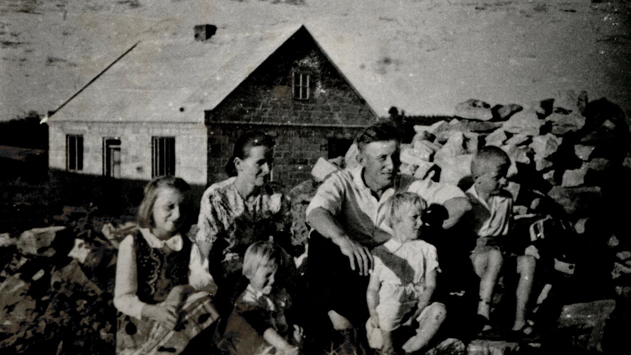 Rodzice z czwórką małych dzieci siedzą przed domem, obok góra cegieł. Archiwalne, czarno-białe zdjęcie.