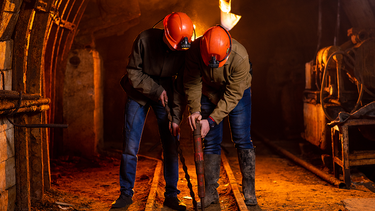Dwóch młodych chłopaków w roboczych mundurach i kaskach ochronnych wykonuje prace w kopalni
