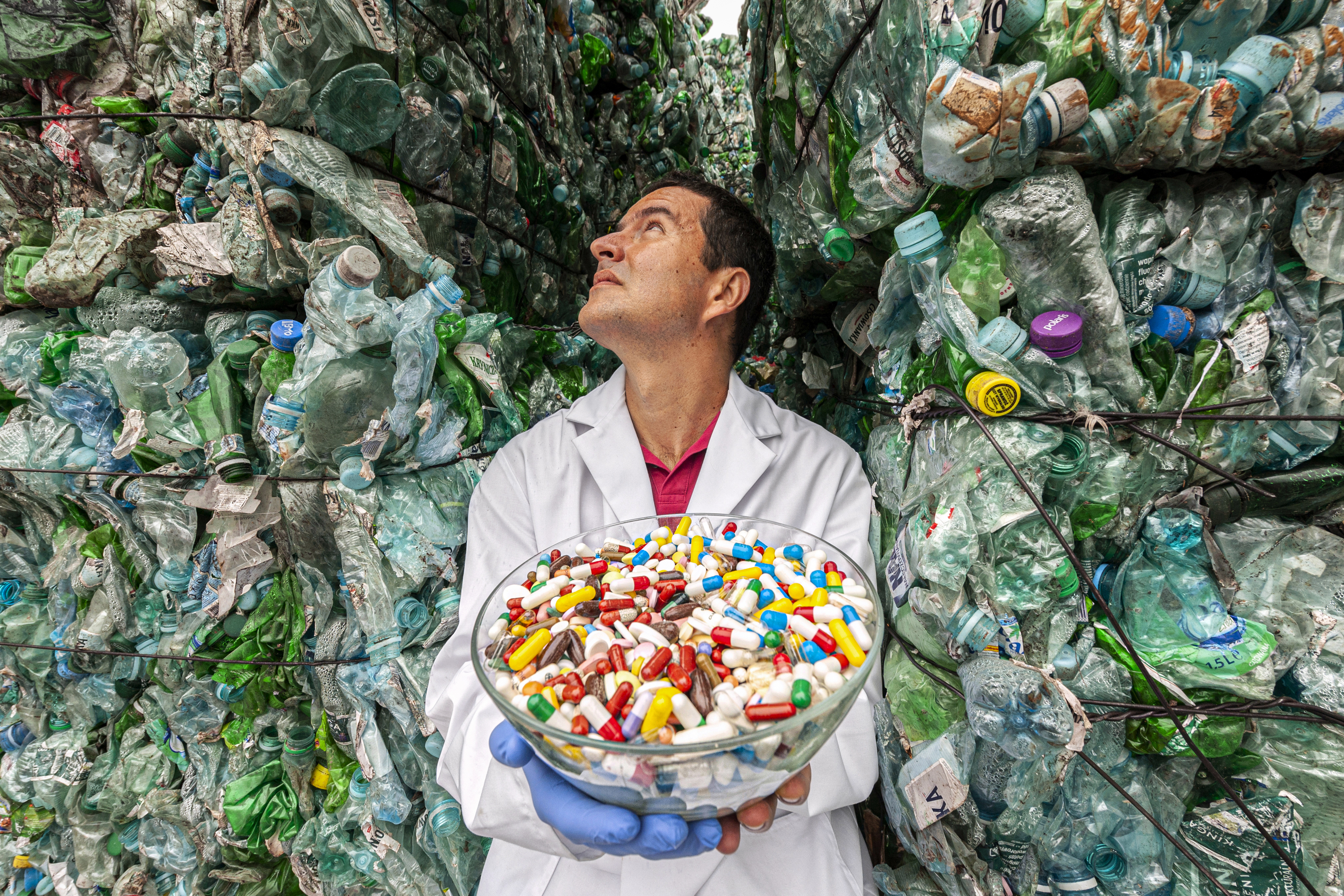 Naukowiec trzyma misę z lekami, w tle góry z plastikowych butelek