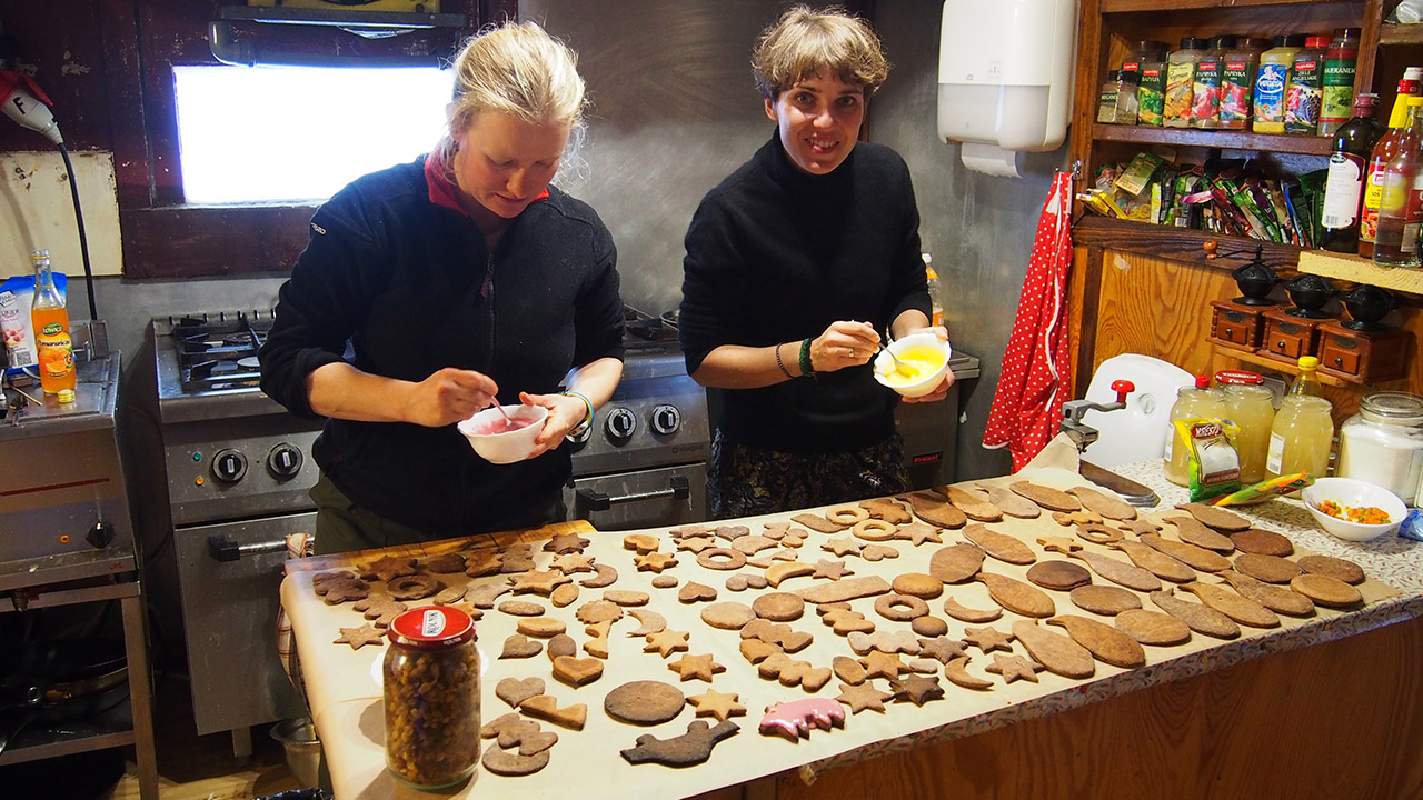 Dwie kobiety pieką pierniki; na kuchennym blacie leży kilkadziesiąt ciastek
