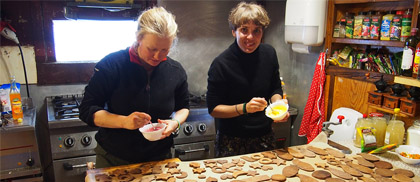 Dwie kobiety pieką pierniki; na kuchennym blacie leży kilkadziesiąt ciastek